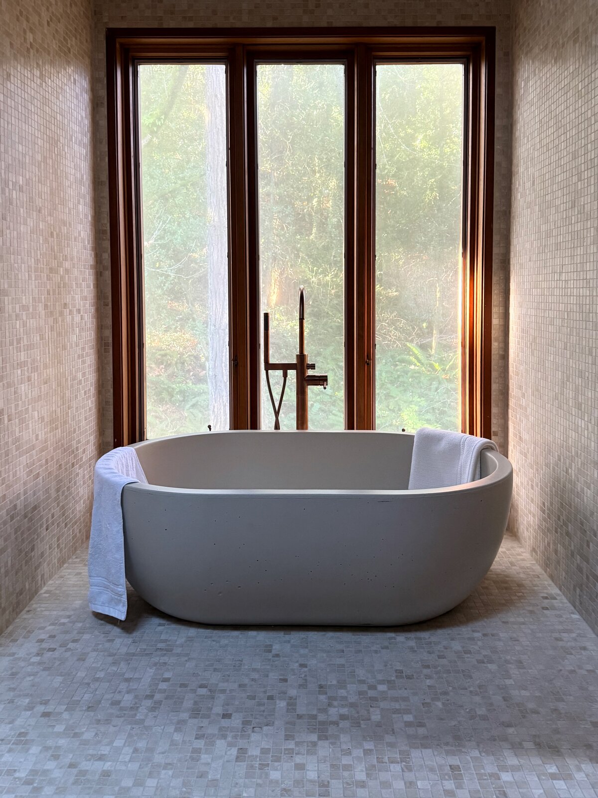 The freestanding tub in the stone mosaic bath, with a window onto the trees.