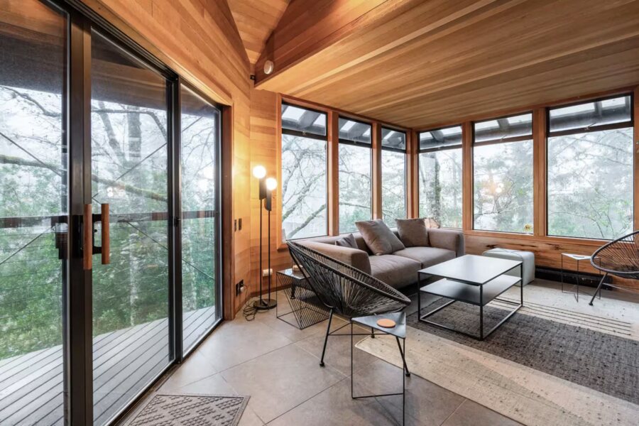 The coast house's living room: cedar walls and ceiling, sliding glass doors to a deck, a wall of windows into the trees.